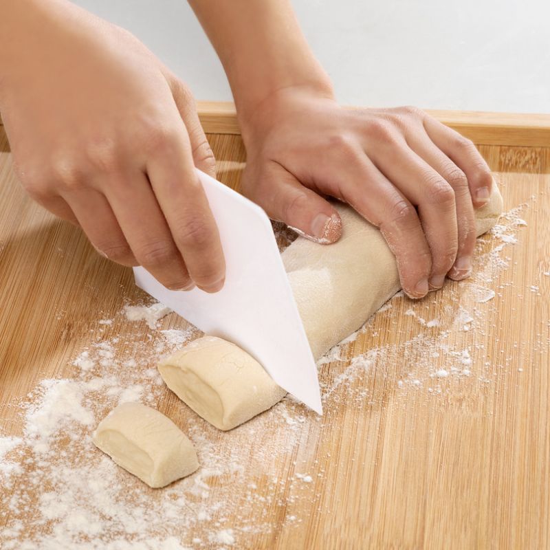 Teig wird auf bemehltem Holzbrett mit Schaber in Stücke geteilt.