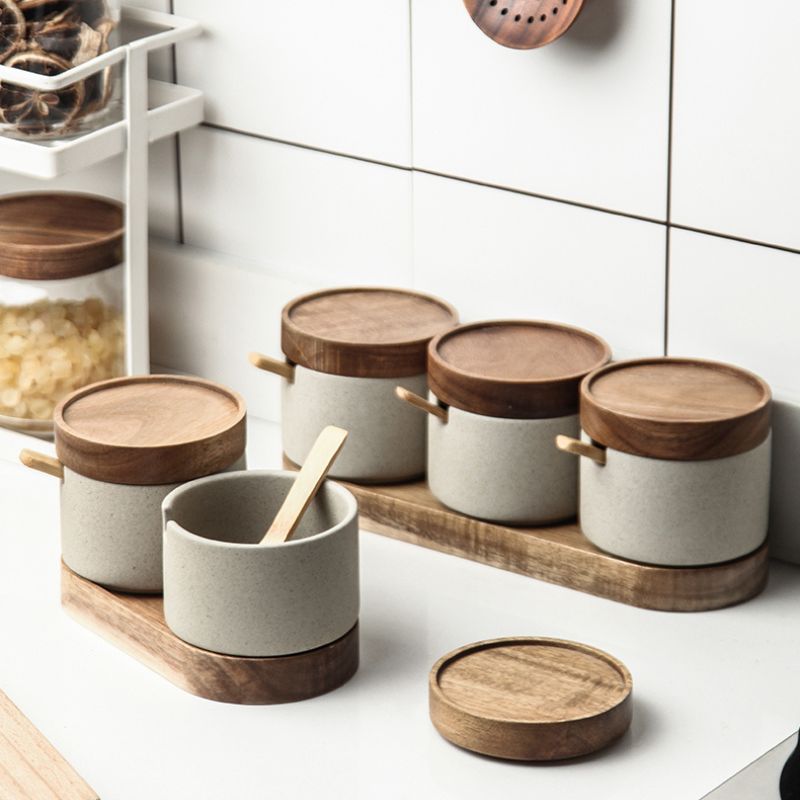 Vier Keramikdosen mit Holzdeckel und Löffel auf einem Holztablett in moderner Küche.