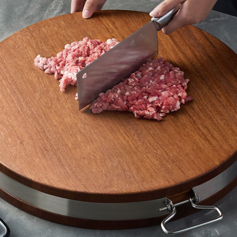 Hackfleisch wird mit einem Messer auf einem runden Holzbrett zerkleinert.