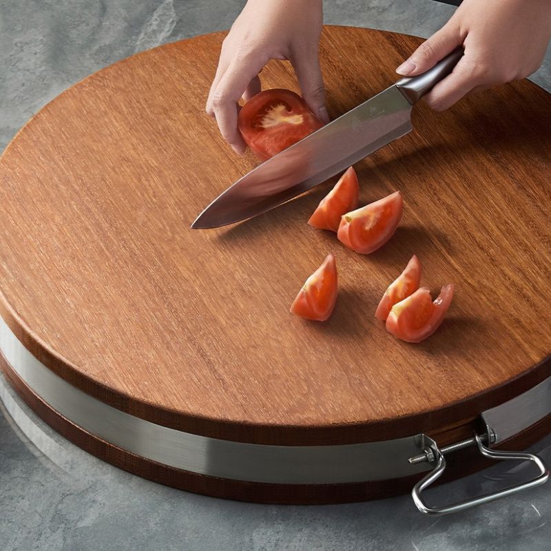 Tomatenstücke werden auf einem runden Holzbrett geschnitten.